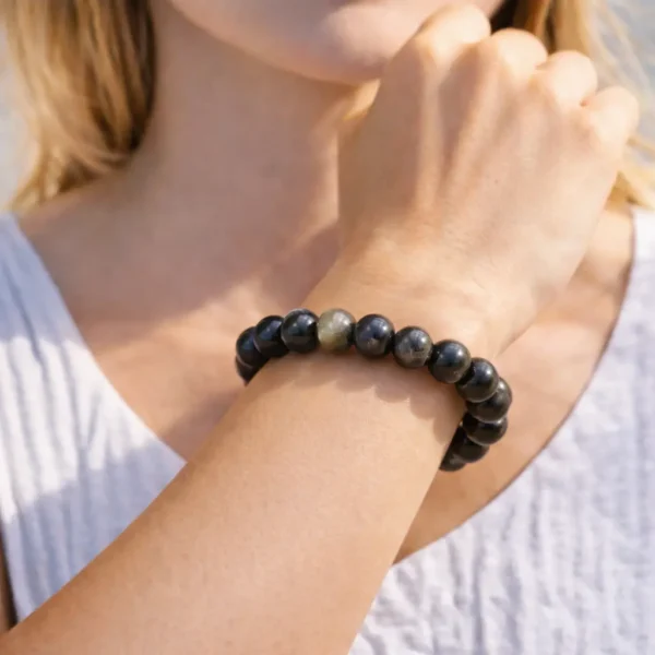 Bracelet en obsidienne dorée naturelle avec reflets scintillants porté au poignet par un mannequin